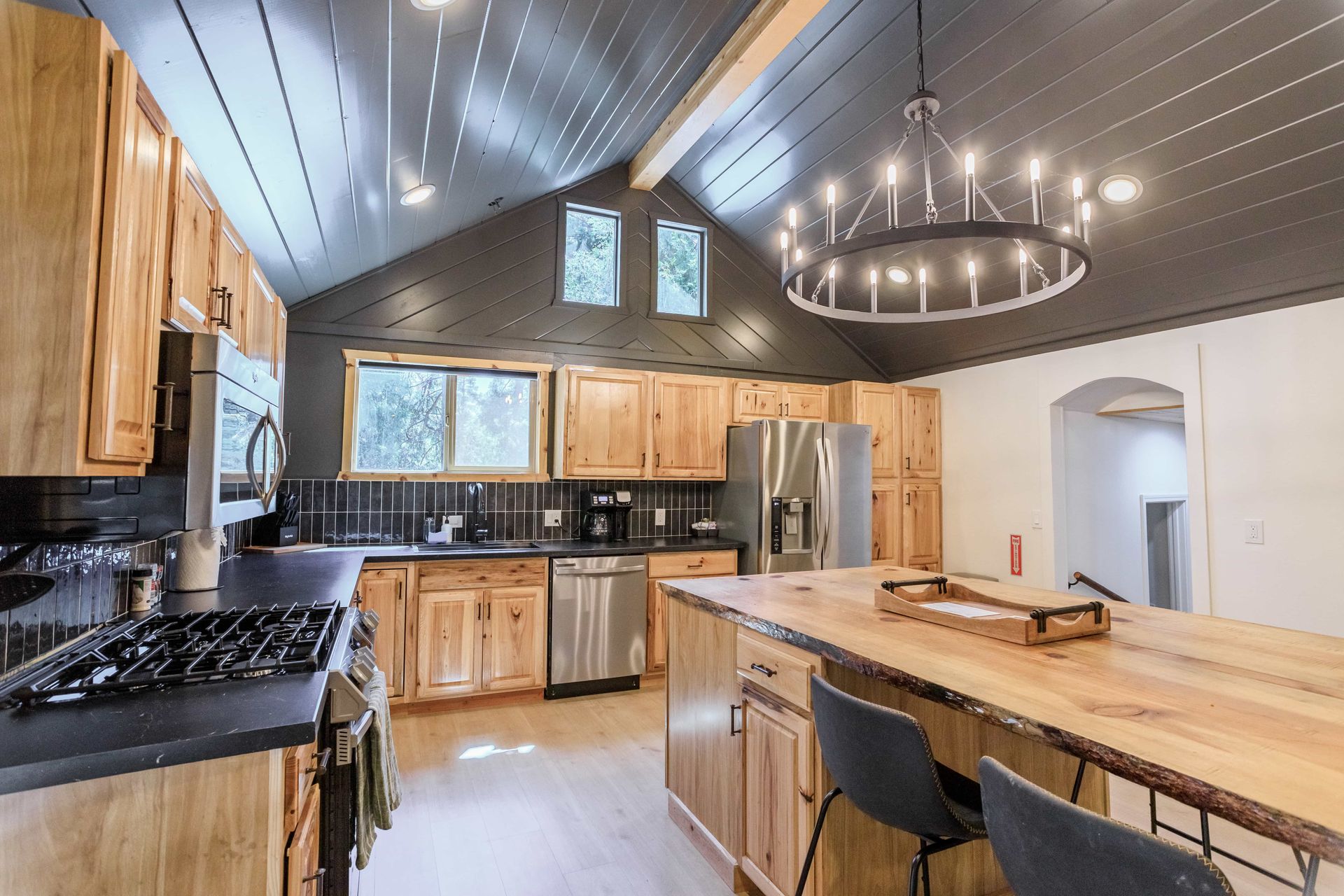 A kitchen with wooden cabinets , stainless steel appliances , a large island and a chandelier.