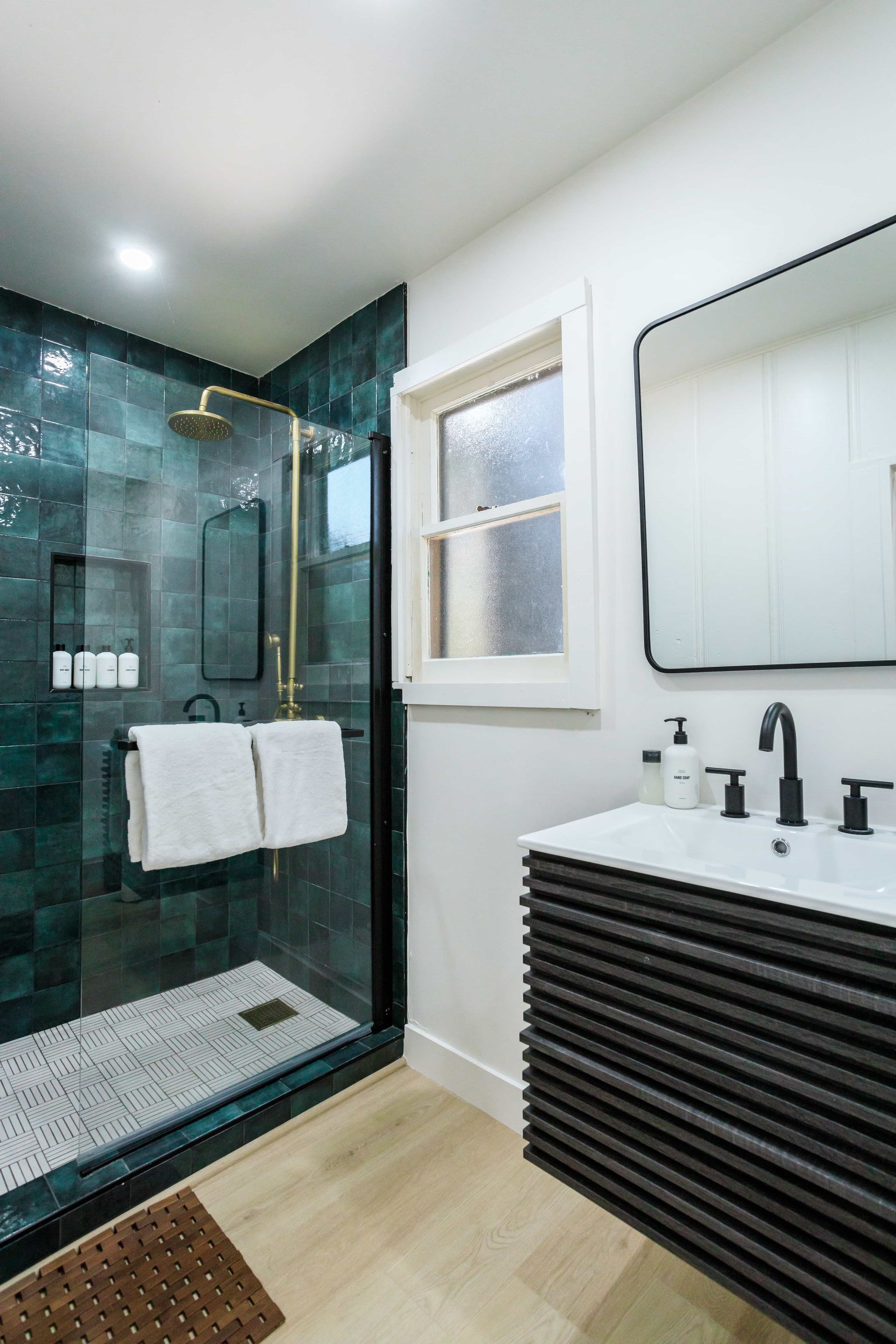 A bathroom with a walk in shower , sink , mirror and window.