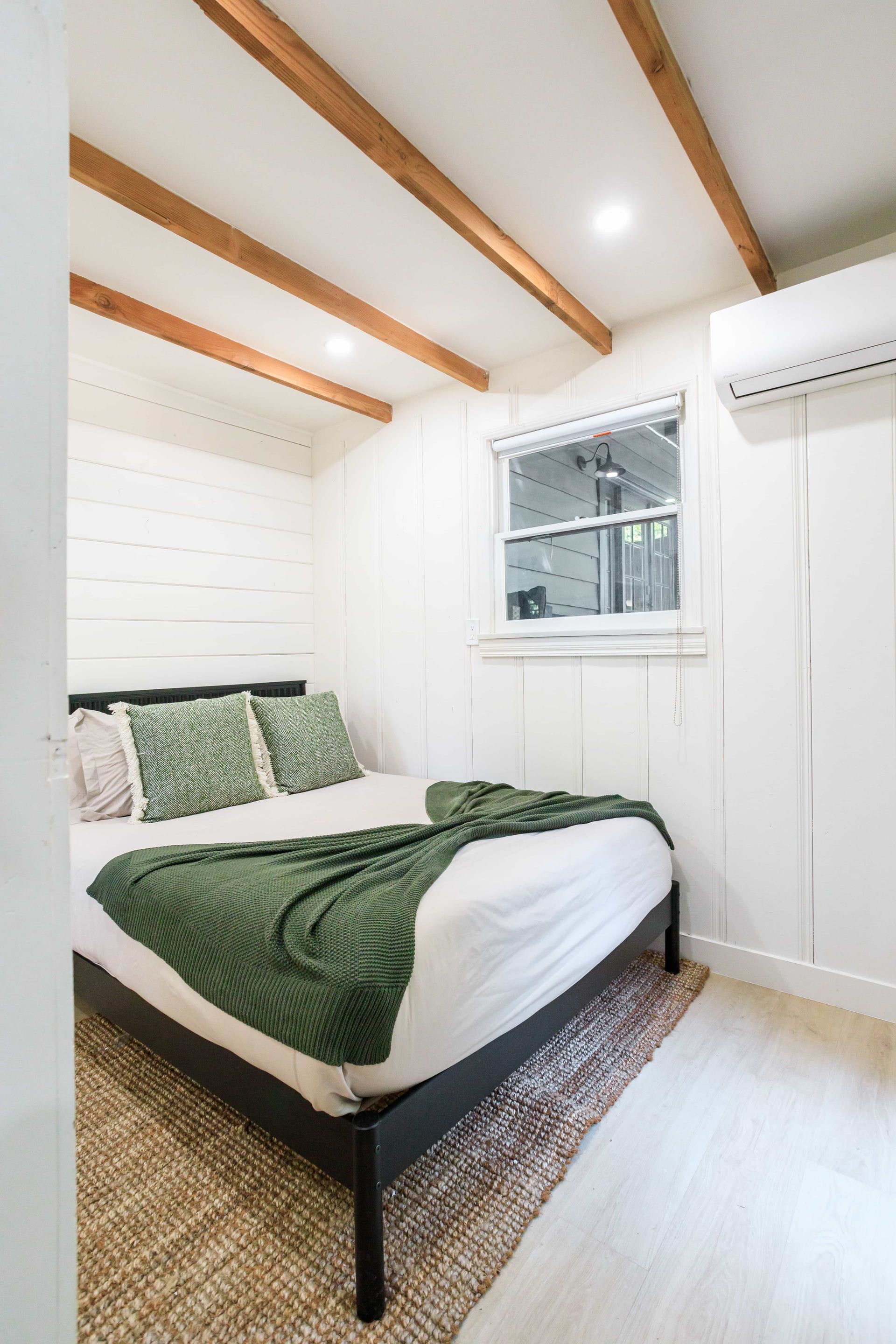 A bedroom with a bed and a window with wooden beams on the ceiling.