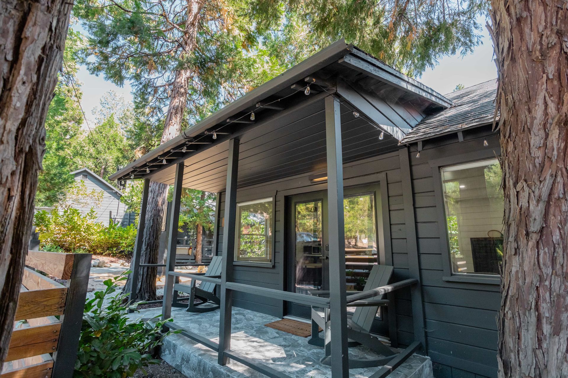 A small black house with a porch surrounded by trees.