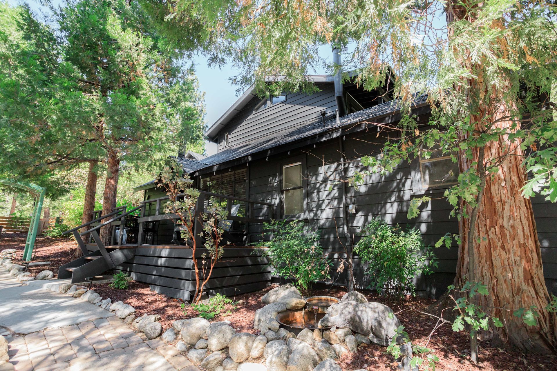 A black house is surrounded by trees and rocks.