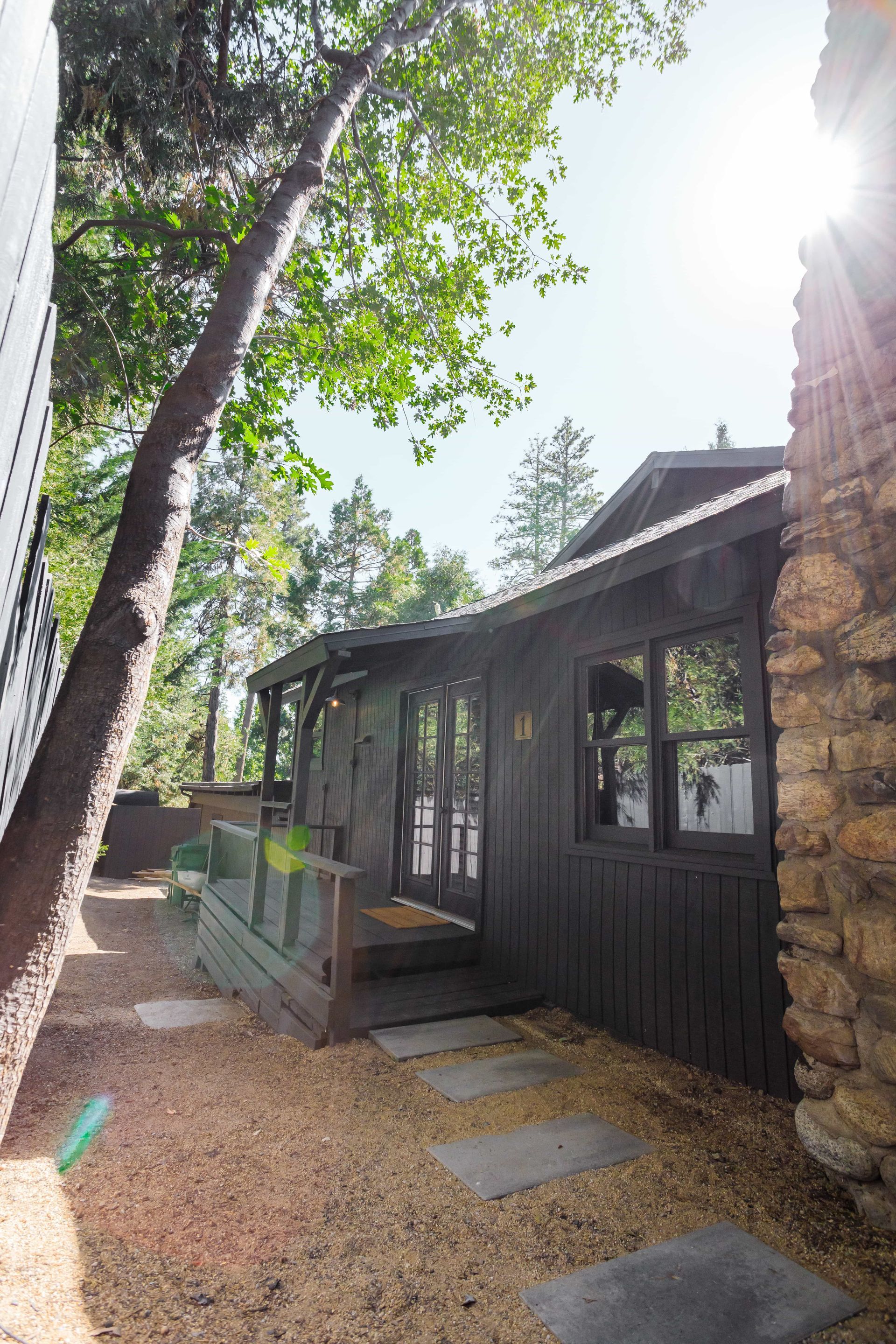 A black house with a stone chimney and a porch surrounded by trees.