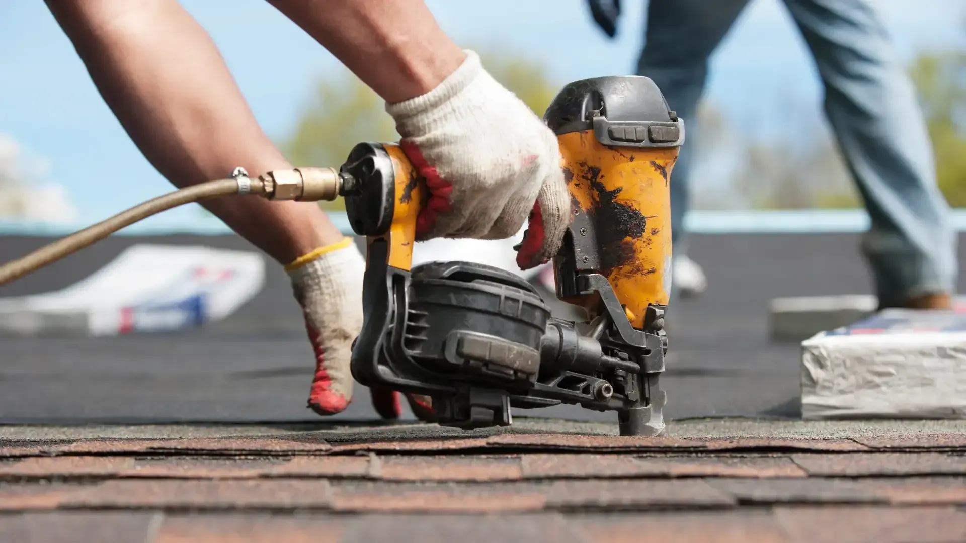 Person using a pneumatic nail gun to install roofing shingles.