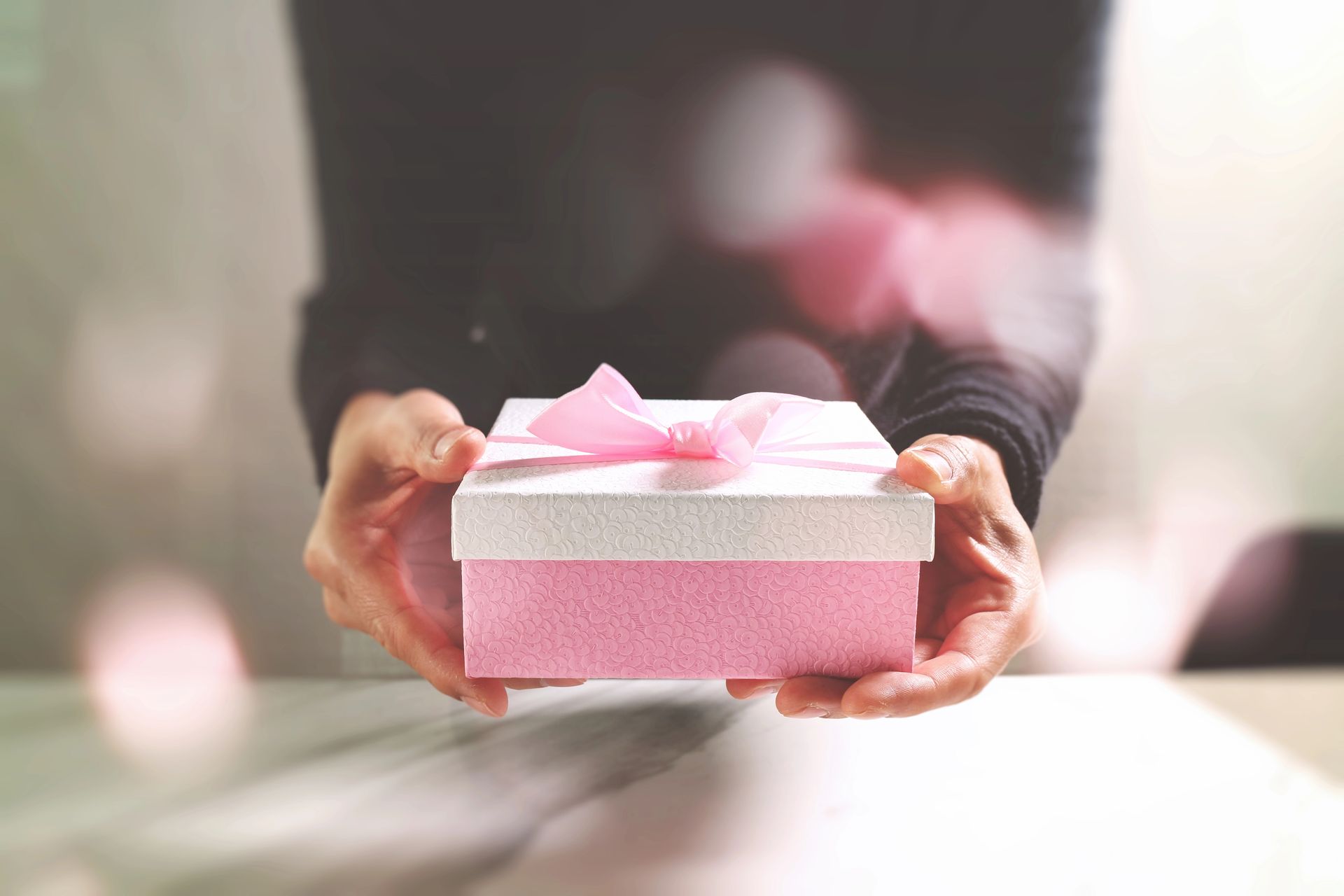 Mani che tengono una scatola regalo rosa con un fiocco rosa, offerta in avanti.