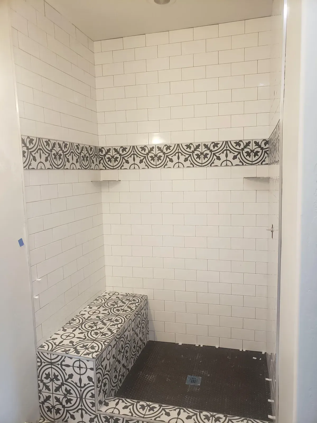 Shower with white subway tile walls, black tile accents, and a built-in bench.