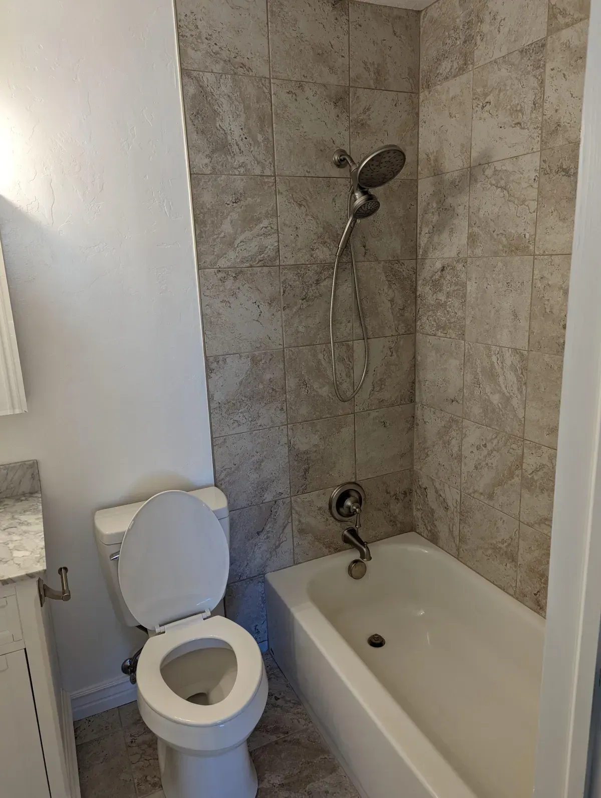 Bathroom with white toilet, tub, and tiled shower wall.