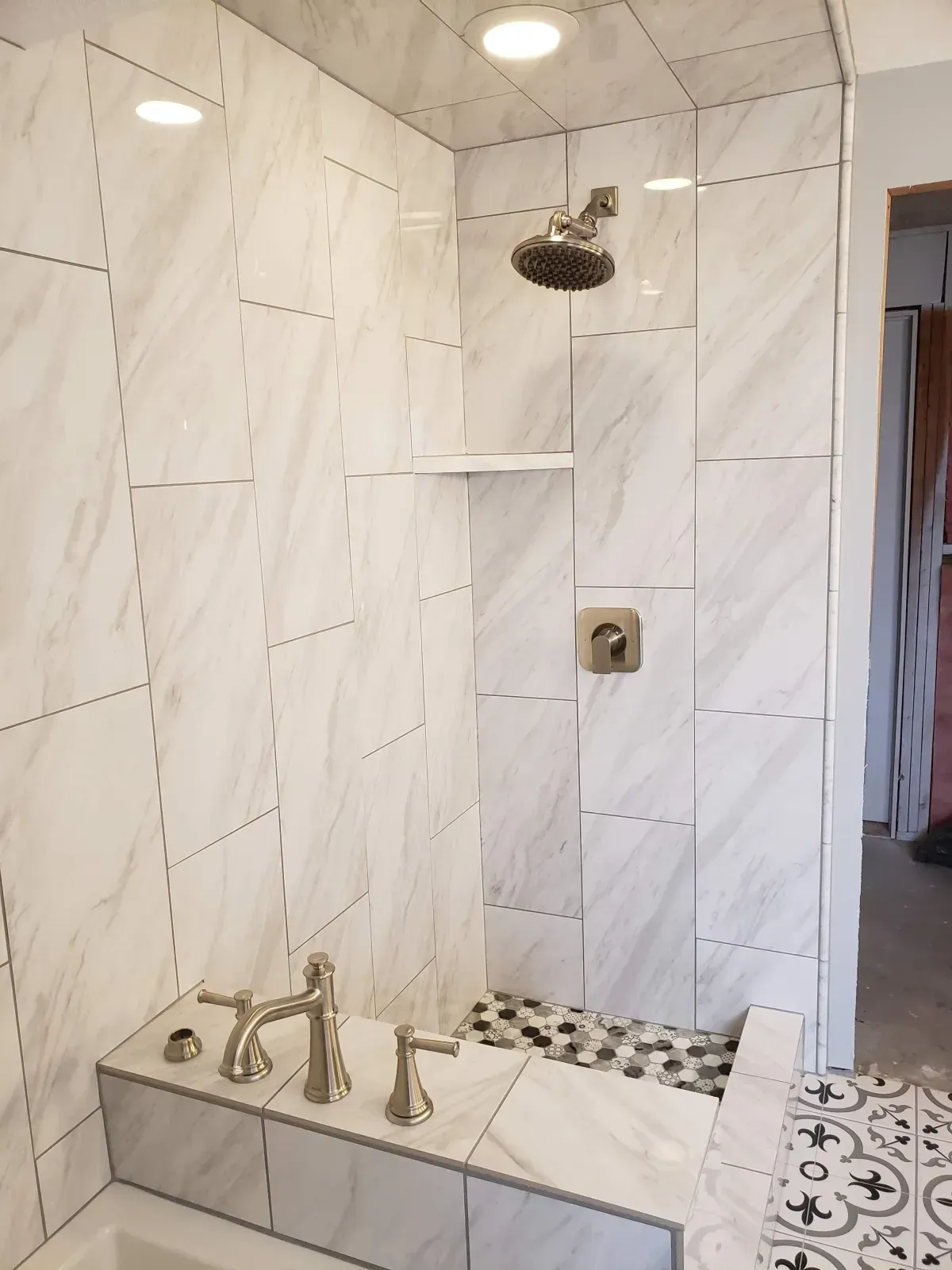 Newly tiled shower with white marble-like tiles, a built-in shelf, and brushed nickel fixtures.