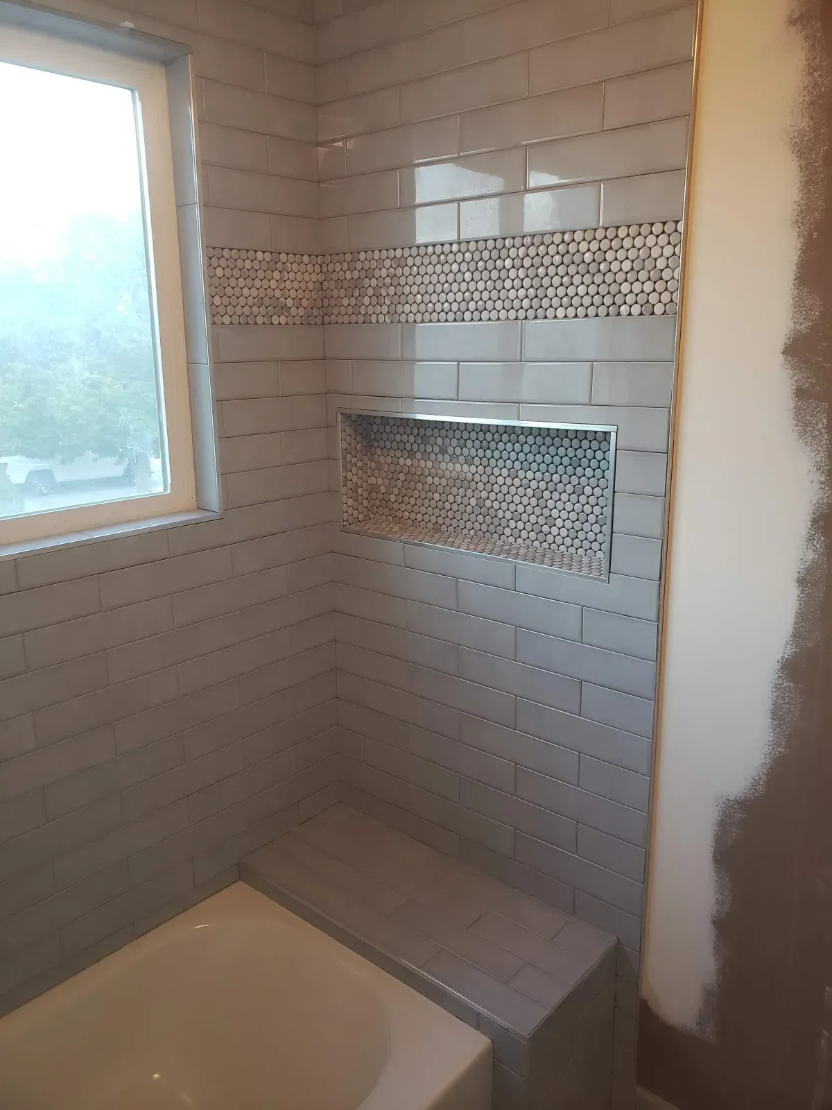 Bathroom with gray tiled walls, recessed shelf, and bathtub.