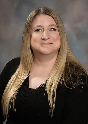 A woman with long blonde hair is wearing a black shirt and smiling for the camera.
