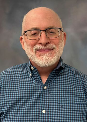 A man with a beard and glasses is wearing a blue plaid shirt.