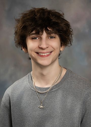 A young man wearing a gray sweater and a necklace is smiling for the camera.