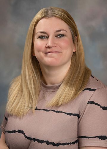 A woman in a pink and black striped shirt is smiling for the camera.