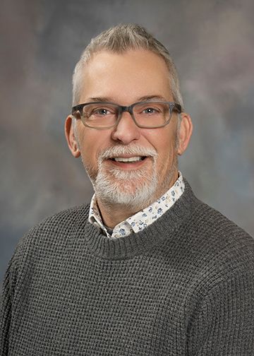 A man with glasses and a gray sweater is smiling for the camera.