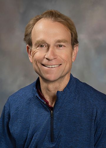 A man in a blue sweater is smiling for the camera.