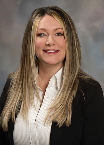 A woman with long blonde hair is wearing a black jacket and a white shirt.