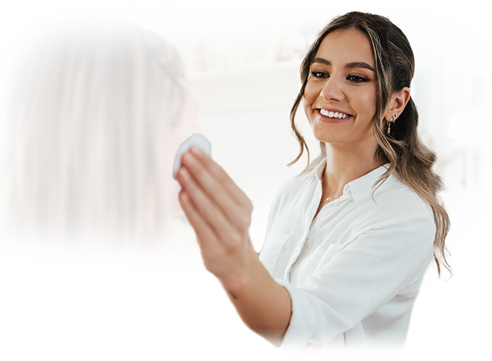 A woman is cleaning her face in front of a mirror.