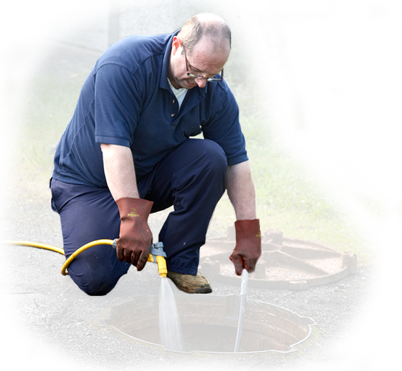 A man is kneeling down in front of a manhole cover