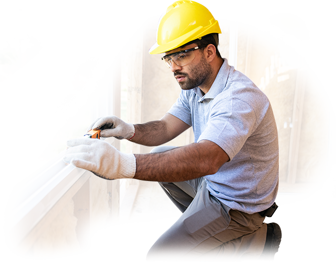 A man wearing a hard hat and safety glasses is working on a window.
