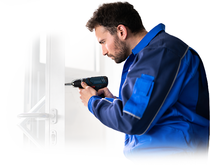 A man in a blue jacket is working on a door with a drill.