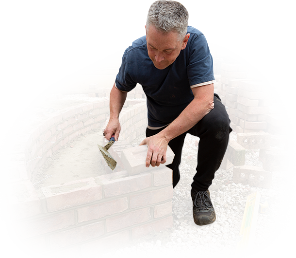 A man is kneeling down to build a brick wall.