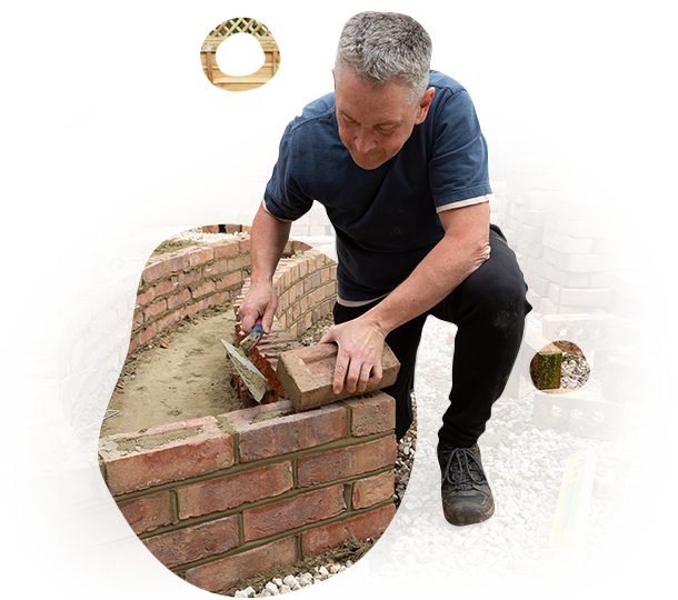 A man is kneeling down to build a brick wall.