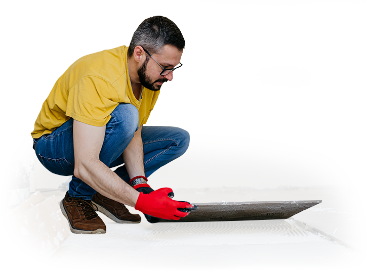 A man is kneeling down and applying adhesive to a tile floor.