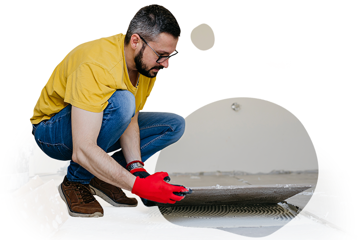 A man is kneeling down and applying adhesive to a tile floor.