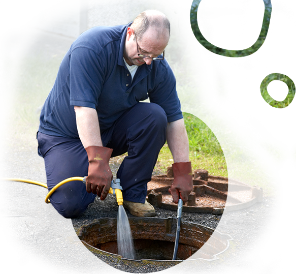 A man is kneeling down in front of a manhole cover