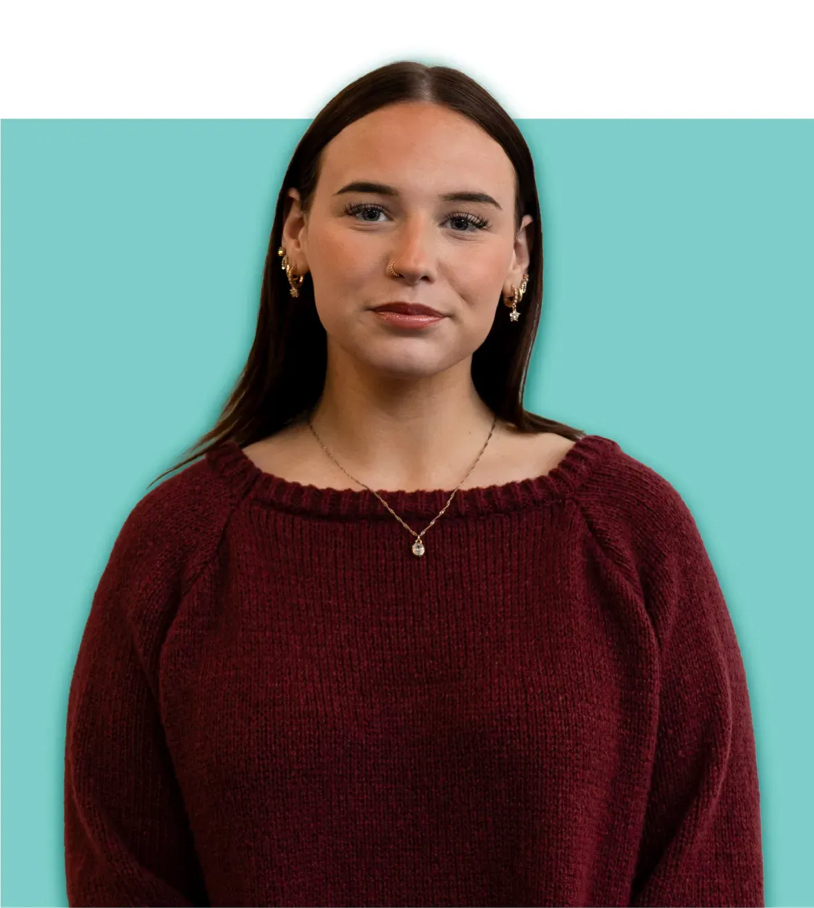 Woman in a burgundy sweater, wearing a necklace and earrings, against a light blue backdrop.