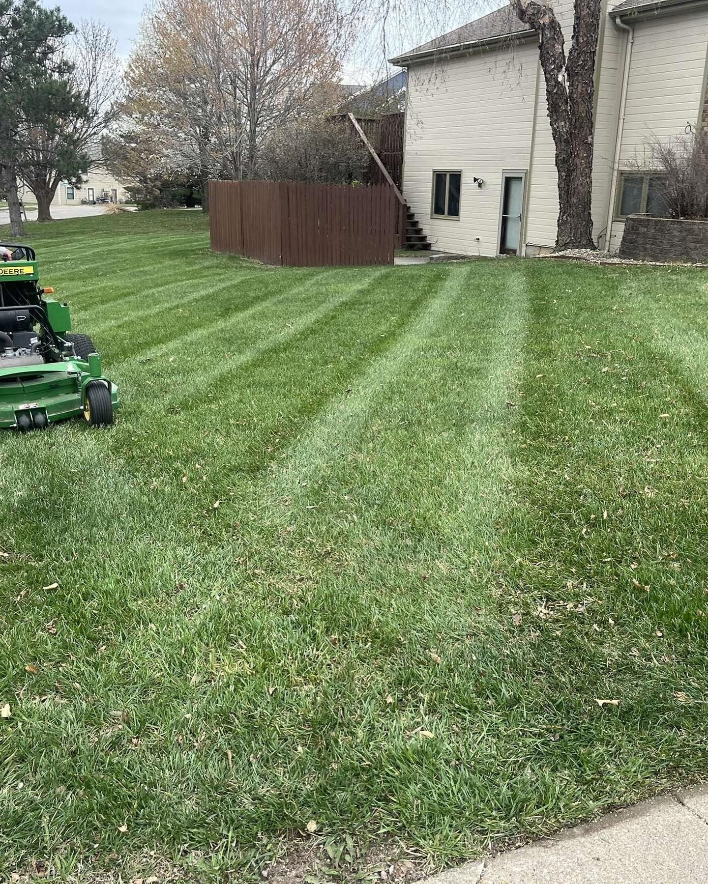 Green lawn freshly mowed with stripes, a mower, a house, and a fence.