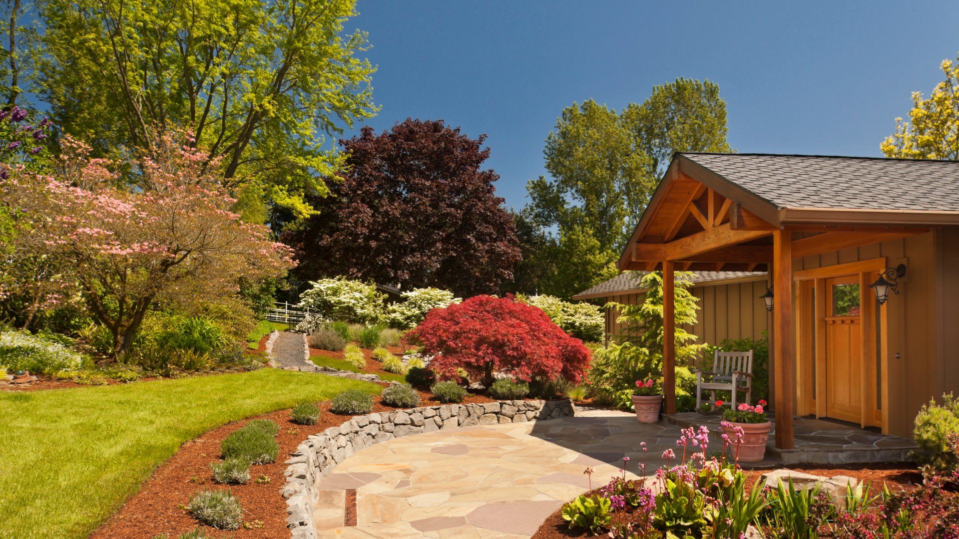 Stamped concrete walkway leading up to a wooden guest house in a backyard.  The walkway is surrounded by nice landscaping.