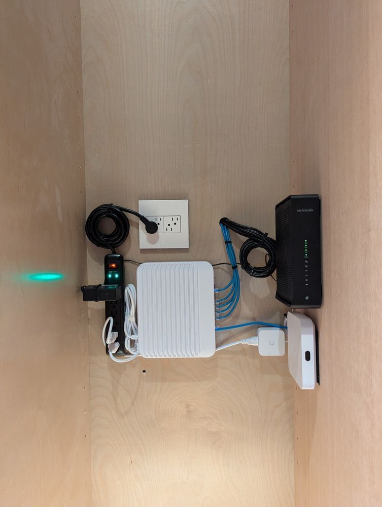 A router is sitting on a wooden wall next to a power strip.
