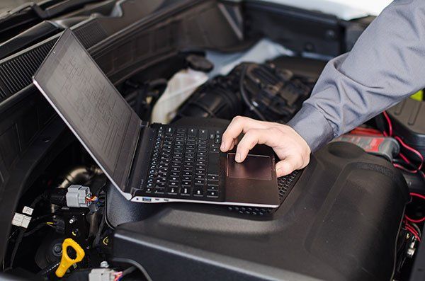 Mechanic with laptop diagnoses car in workshop