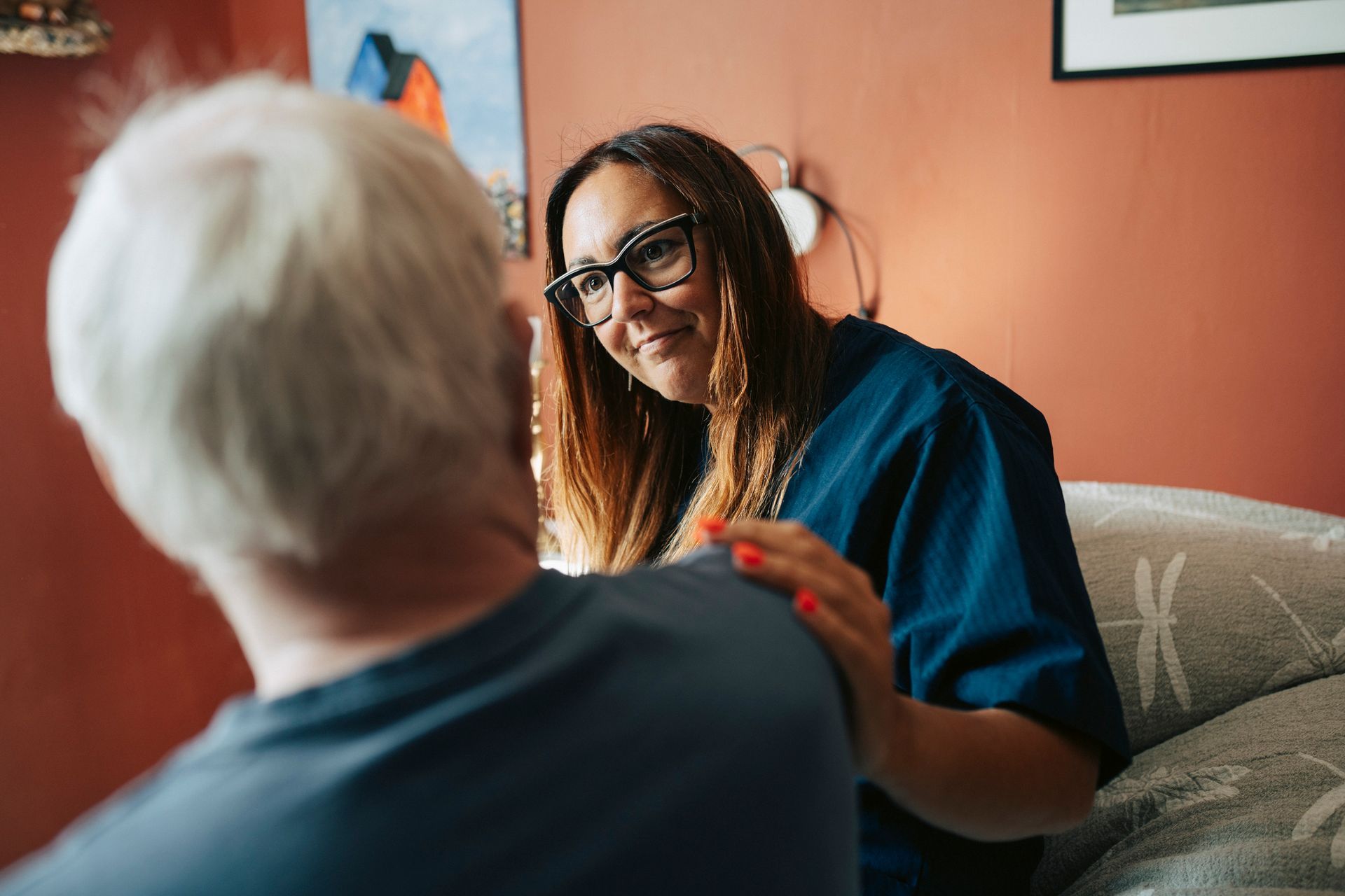 Smiling female caregiver wearing eyeglasses consoling a senior man in his home.