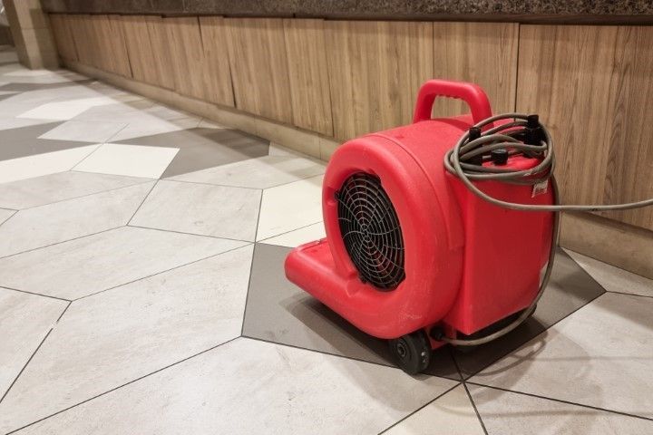 Red air mover on patterned tile floor near wood paneling.
