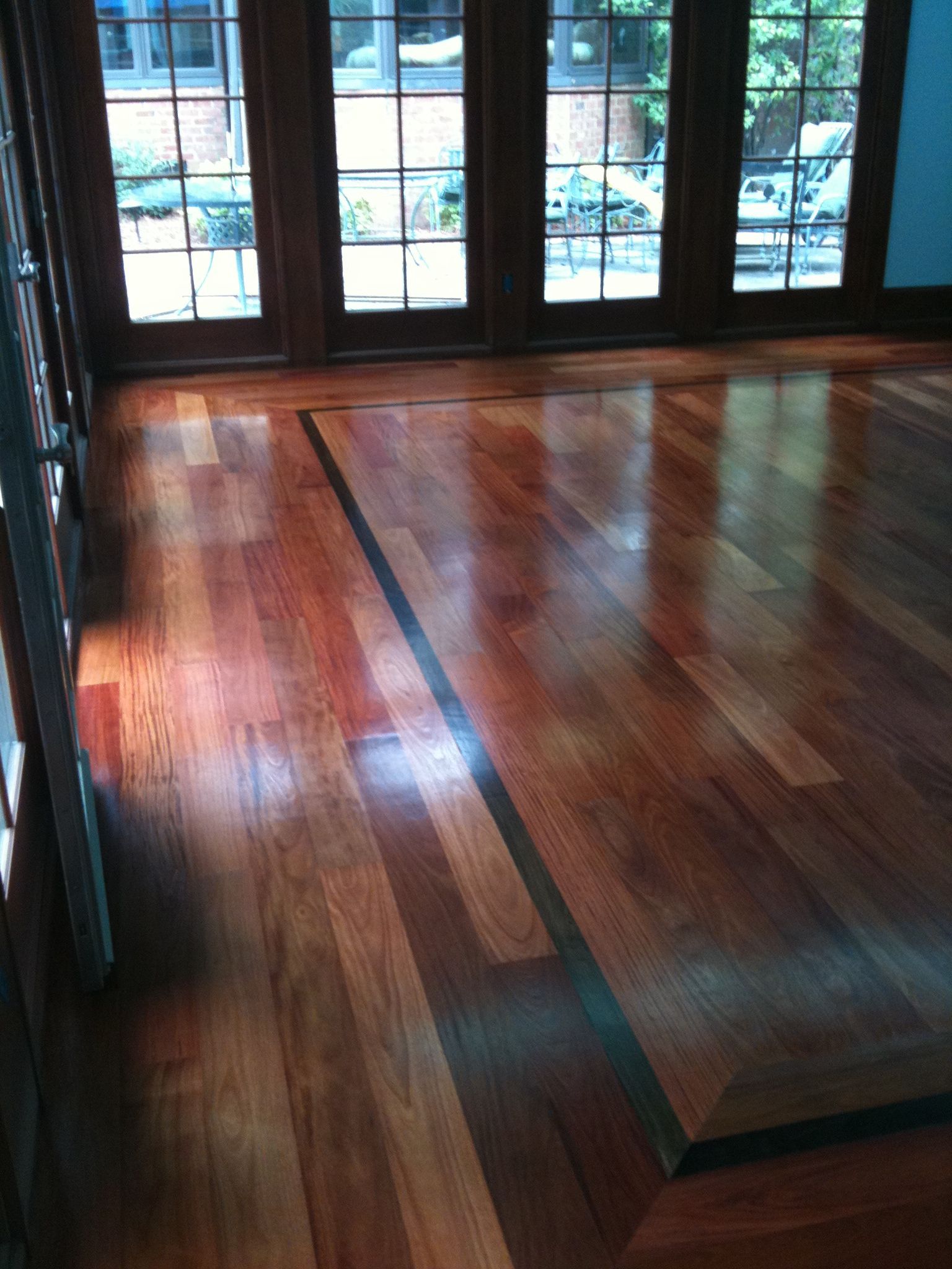 Shiny hardwood floor with a raised platform, in front of glass doors and windows.