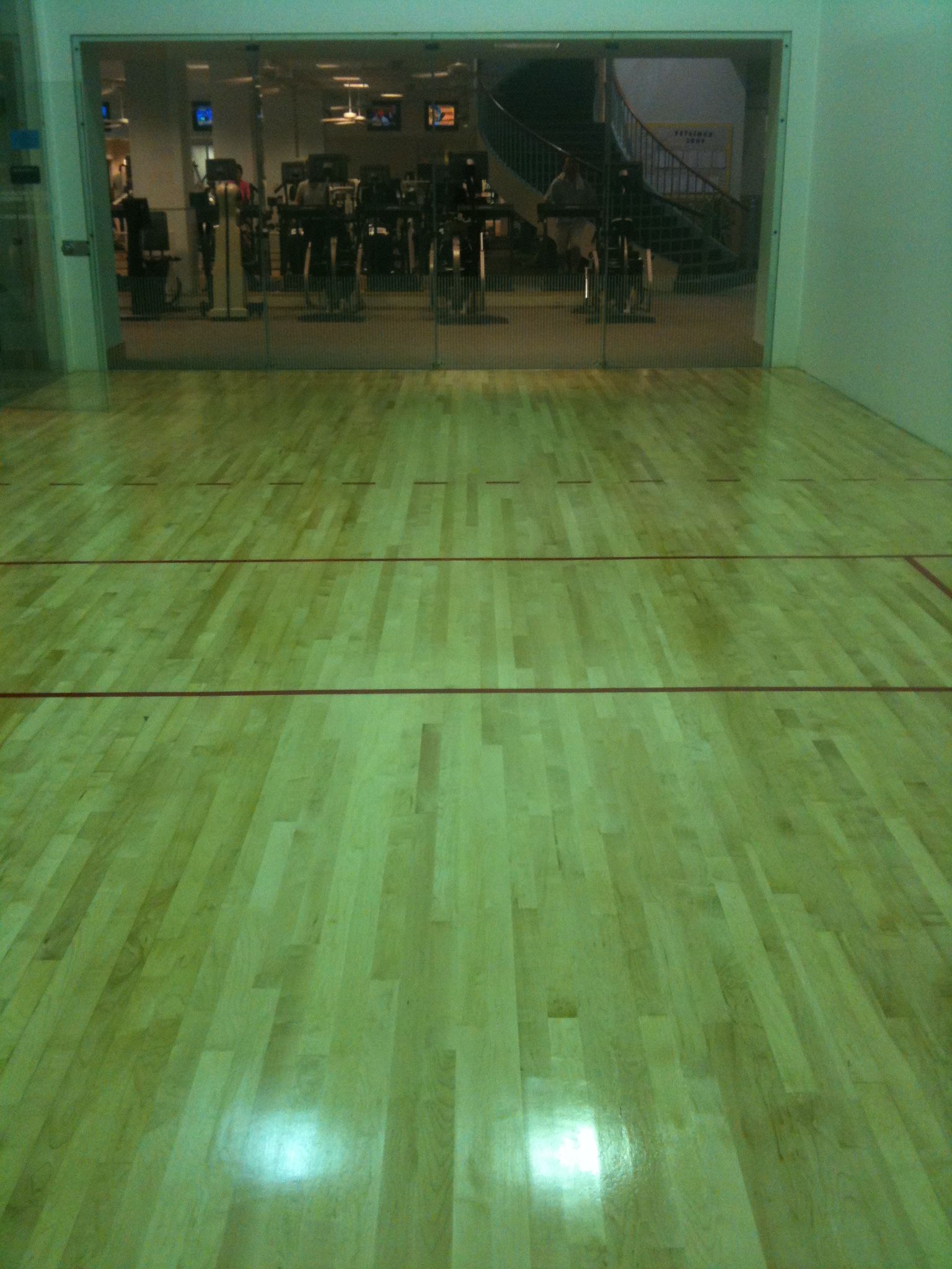 Empty indoor basketball court with polished wooden floor and a glass wall at the far end.