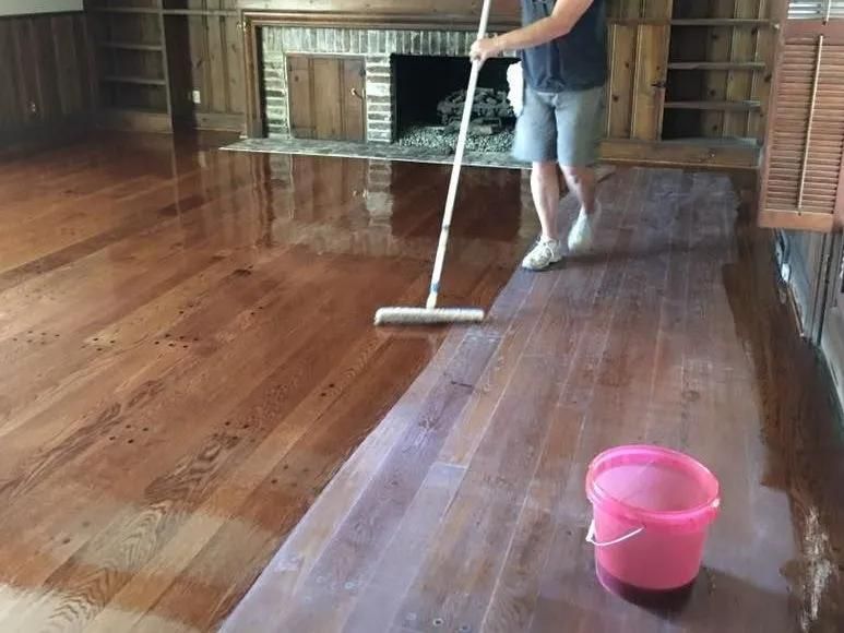 Person mopping a shiny wooden floor beside a pink bucket in a room with a fireplace.