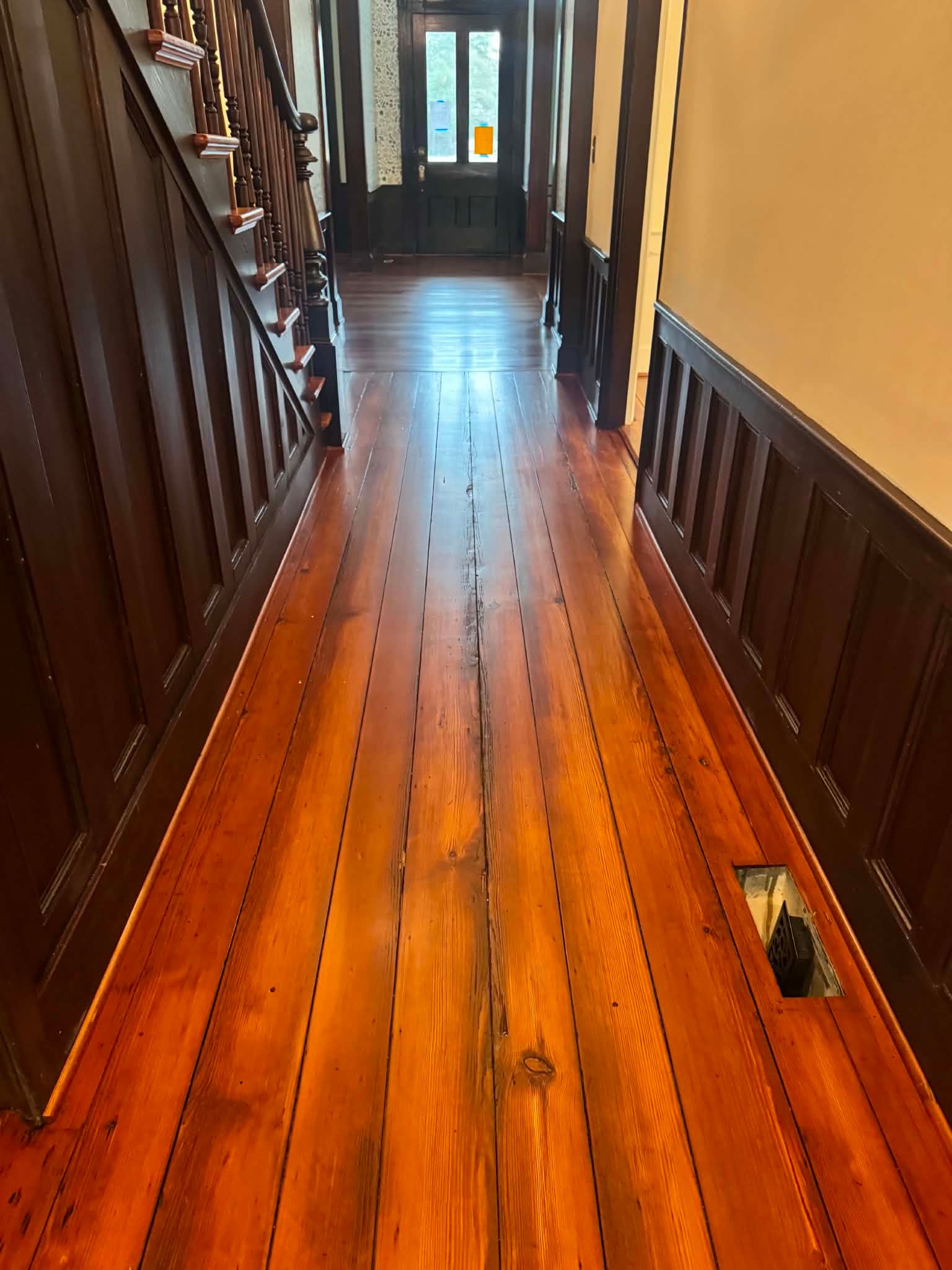 Narrow wooden hallway with polished floor, dark trim, and a window at the far end.