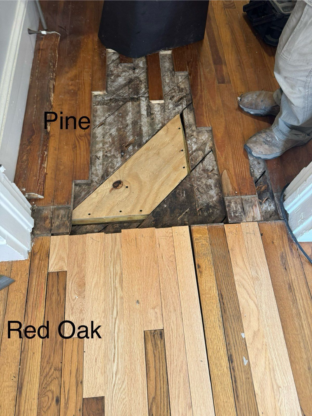 Flooring transition showing pine and red oak boards with exposed subfloor in a doorway.