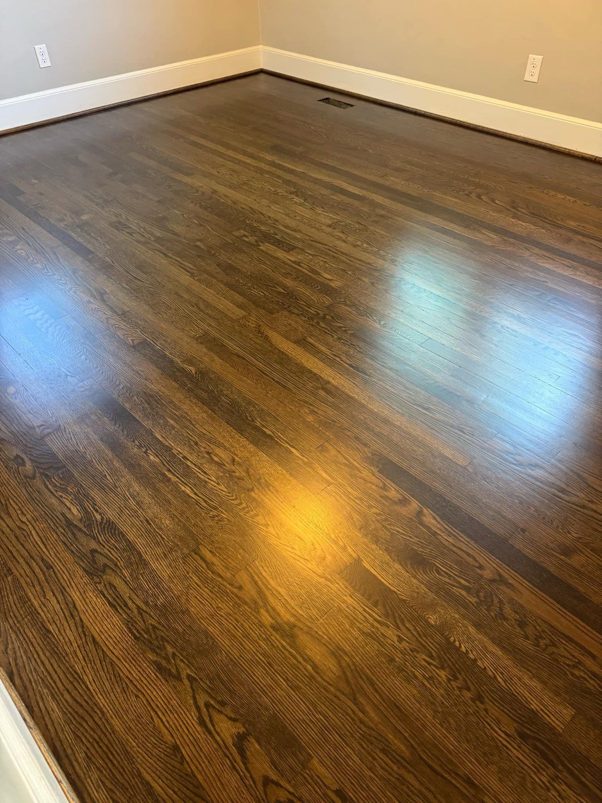 Empty room with dark wood flooring and beige walls, lit by sunlight reflections