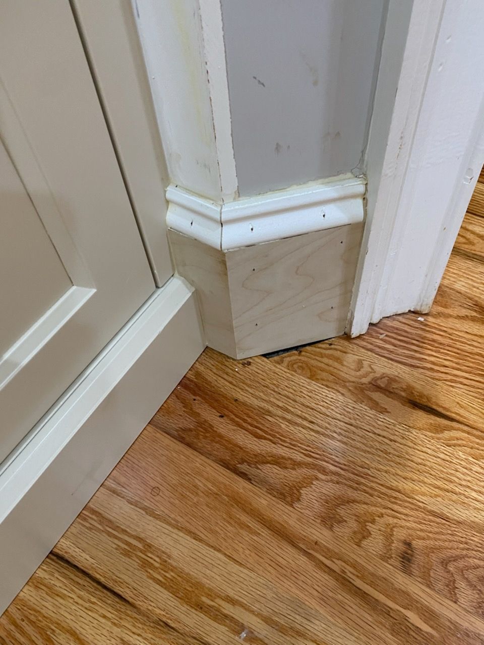 Close-up of a corner where a white baseboard meets a door frame over hardwood flooring.