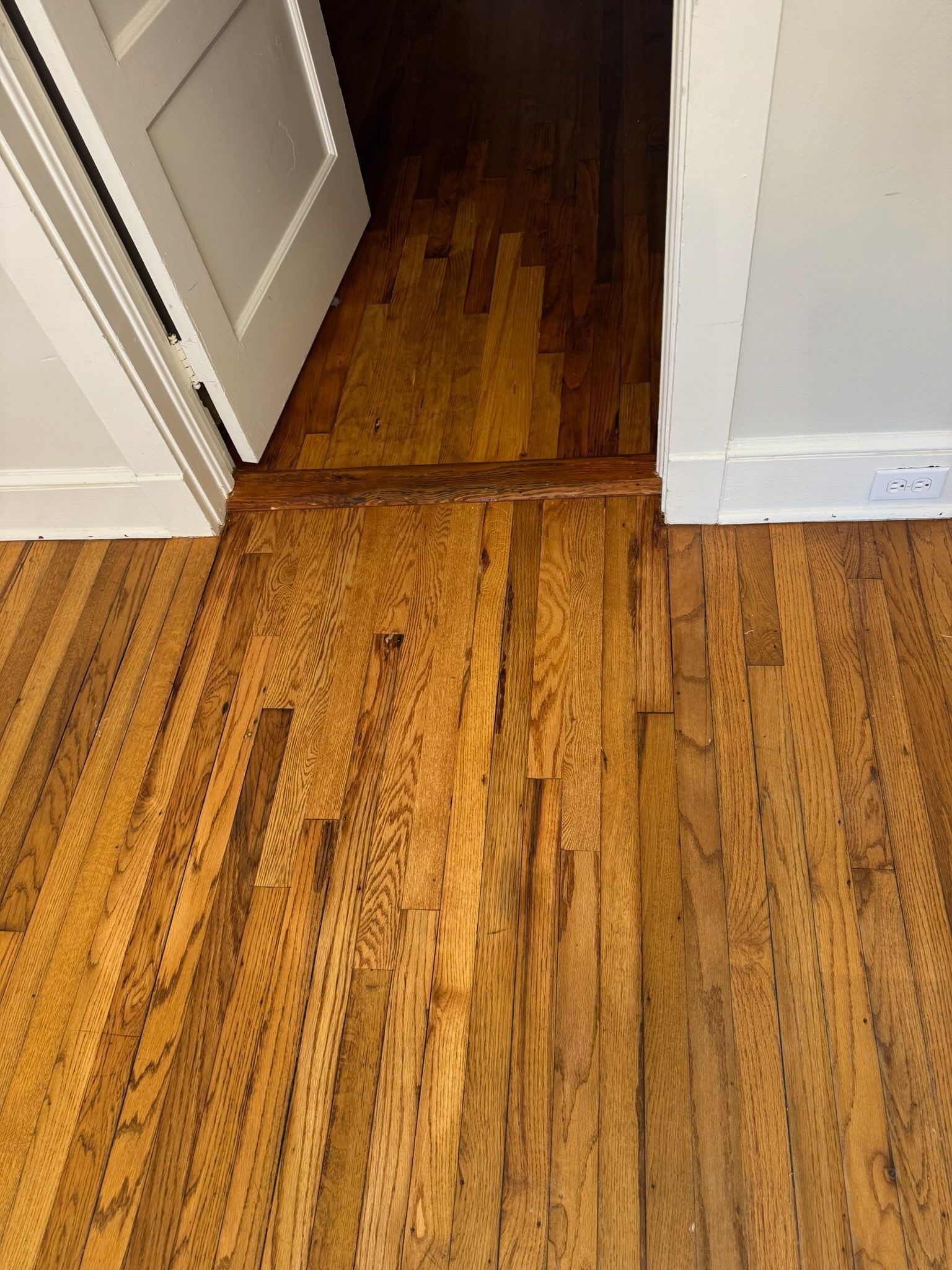 Wooden floor with visible worn or damaged transition strip in a doorway between rooms