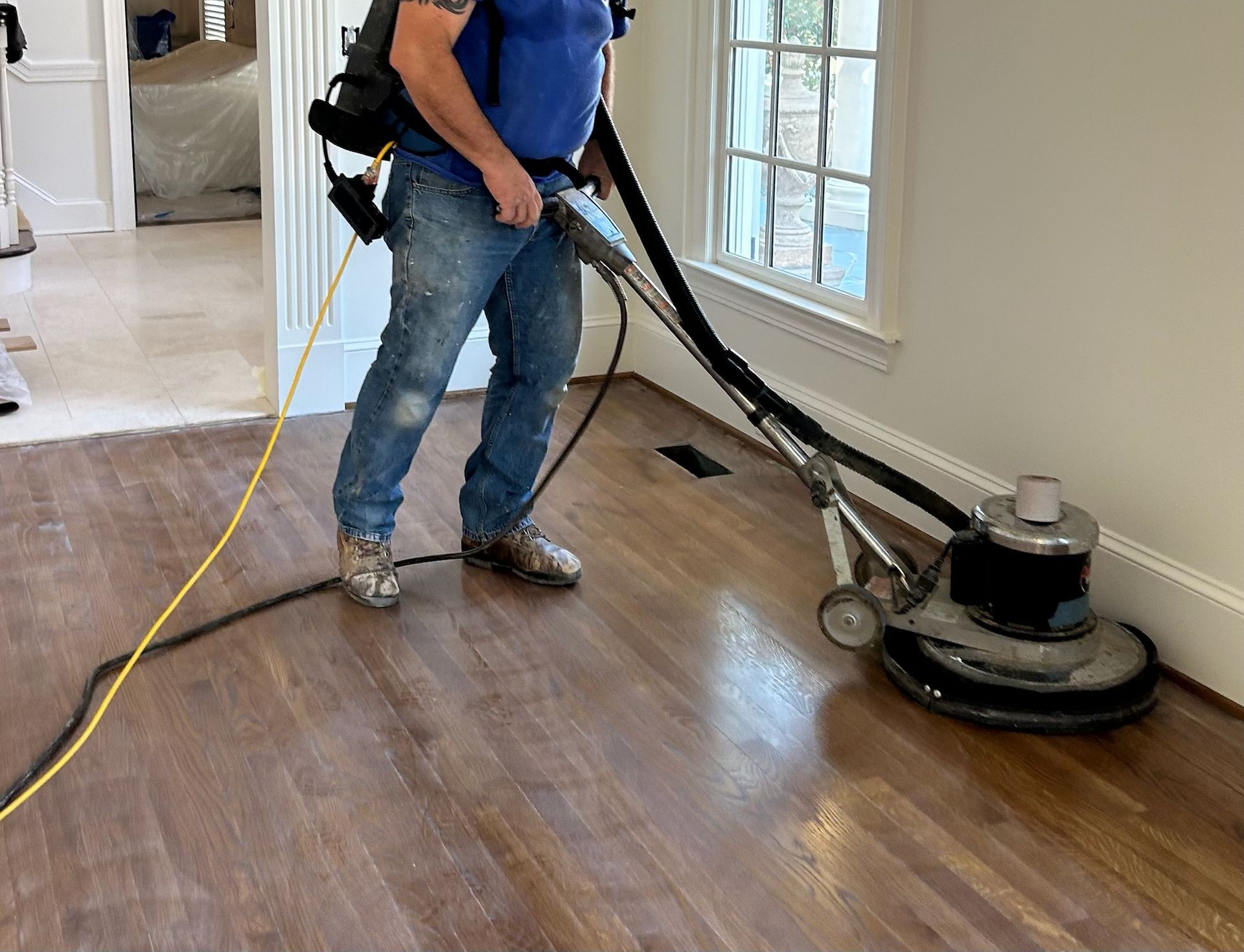 Worker sanding a hardwood floor with a floor buffer in a bright room