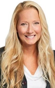 Blonde woman smiling, wearing a black blazer and white top, against a white backdrop.