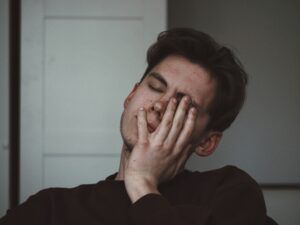 A young man is covering his face with his hand.