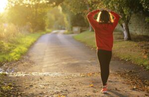 A woman is walking down a road with her hands on her head.