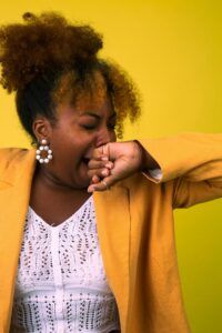 A woman in a yellow jacket is covering her mouth with her hand.