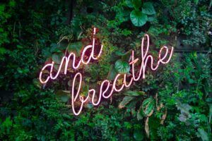 A neon sign that says `` and breathe '' is surrounded by green plants.