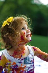 A little girl is covered in paint and smiling.